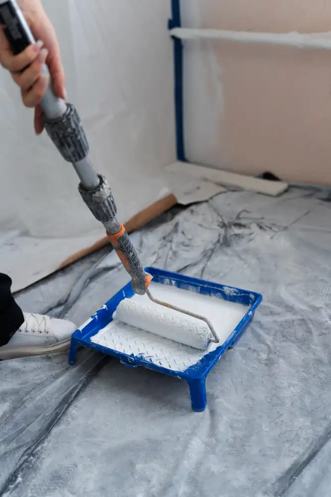 Rodillo con pintura blanca en bandeja durante trabajo de pintura interior