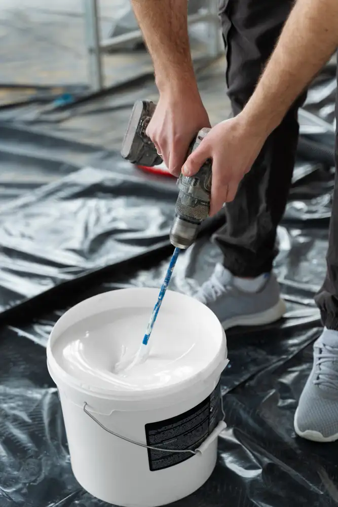 Trabajador mezclando pintura blanca en balde para trabajo de pintura interior