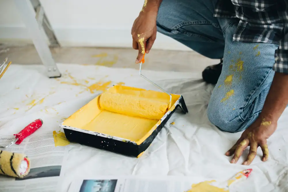 Rodillo con pintura amarilla sobre bandeja durante trabajo de pintura interior