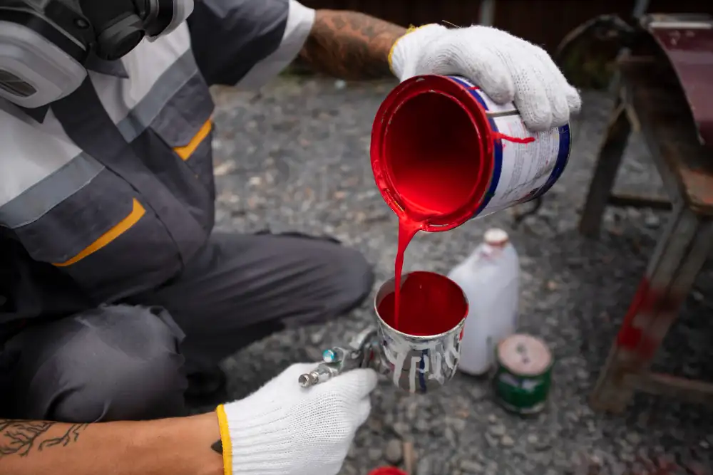 Trabajador preparando pintura roja para aplicar terminaciones con pistola pulverizadora