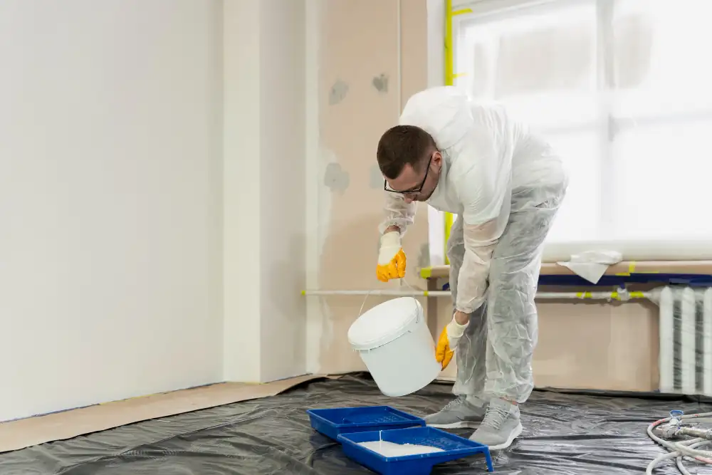 Trabajador preparando pintura blanca en interior protegido para pintar muros